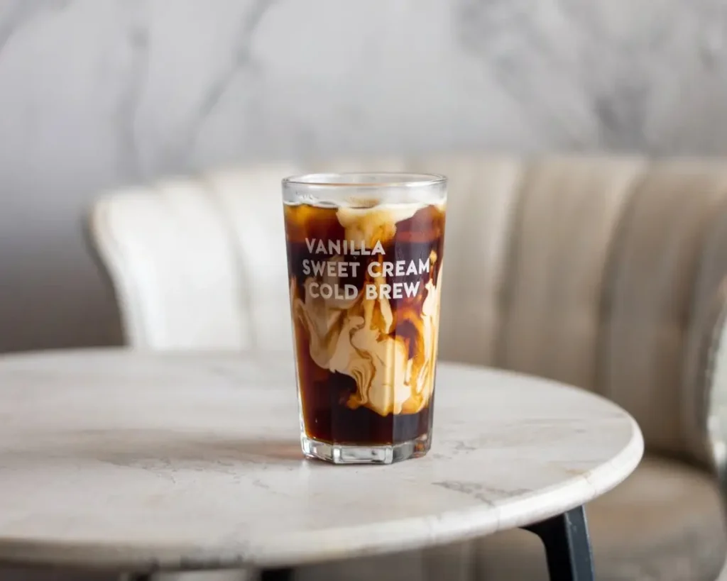 A tall glass of vanilla sweet cream cold brew with swirling cream and condensation